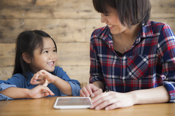 Mother and daughter are using a digital tablet at the table together.
