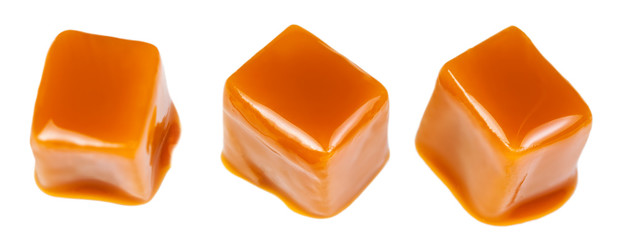 Caramel sauce flowing on caramel candies, isolated on white background. Golden Butterscotch toffee...