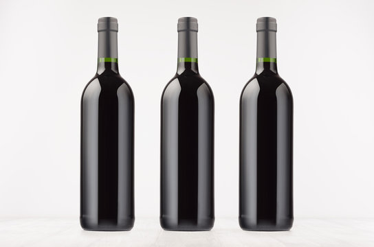 Three black wine bottles with red wine on white wooden board, mock up. Template for advertising, design, branding identity.