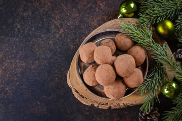 Homemade chocolate truffles on the paper on stone concrete table background with festive holiday decoration. Christmas Dessert