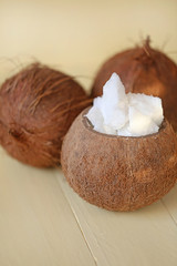 Natural coconut oil. Coconut in a cut and coconut oil  in a brown wooden cup on a yellow wooden board background