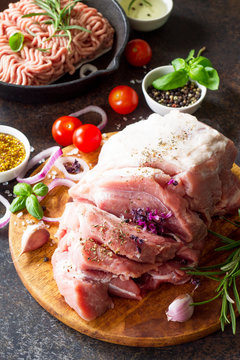 Pork fillet on a cutting board, raw meat, assorted minced pork and beef and various spices on a stone or slate background.