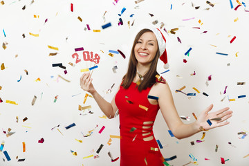 Pretty caucasian young happy woman with charming smile in red dress and Christmas hat holding card number 2018 on white background, colorful confetti. Santa girl isolated. New Year holiday concept