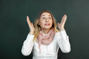 Picture of emotional blonde senior woman teacher wearing elegant yellow scarf wrapped around her neck gesturing actively with both hands while exclaiming, telling off her mischievous students