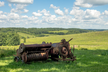 Obraz premium Rusty Baler with Rolling Hills in the Background