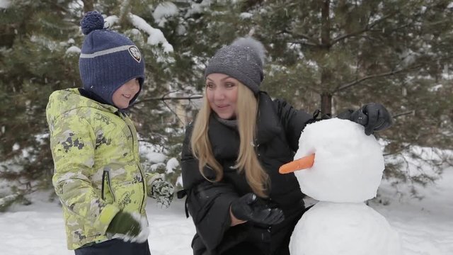 Mom and son make a snowman 4 Happy mother and son make a snowman falling fluffy snow