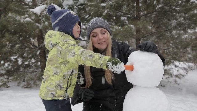 Mom and son make a snowman 5 Happy mother and son make a snowman falling fluffy snow