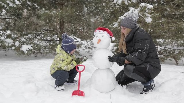 Mom and son make a snowman 11 Happy mother and son make a snowman falling fluffy snow