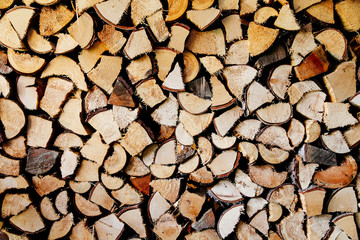 Stack of round and square natural firewood in preparation for the winter and used for camp fires, fireplaces and home heating. Chopped and piled wood background texture.