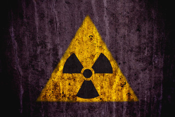 Obraz premium Triangular yellow and black radioactive (ionizing radiation) danger symbol painted on a massive concrete wall with dark rustic grunge texture background.