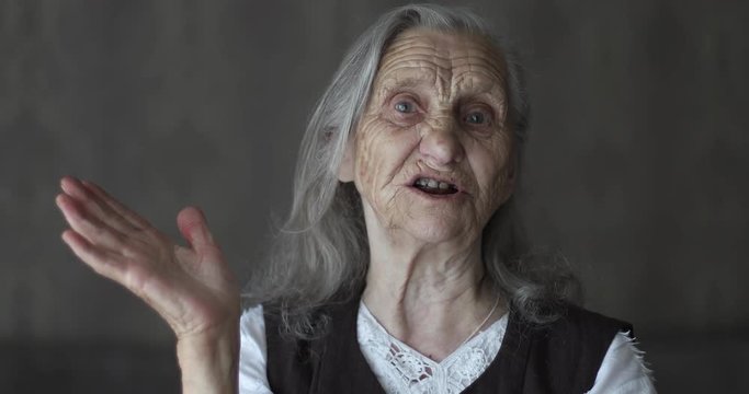 Portrait of old woman with grey hair telling story and gesticulating hands.