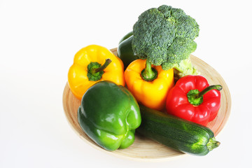 Green,red and yellow bell pepper with broccoli and zucchini on wooden plate