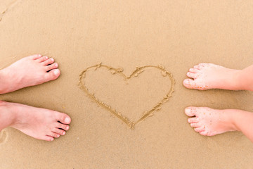 legs loving couple barefoot on the sand near the heart pattern