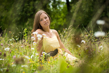 Beautiful woman enjoys nature in summer bloom. Lonely girl has a beautiful face. The woman sits in the meadow. Blurry background.