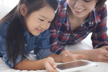 Mother and daughter are using a digital tablet at the table together.