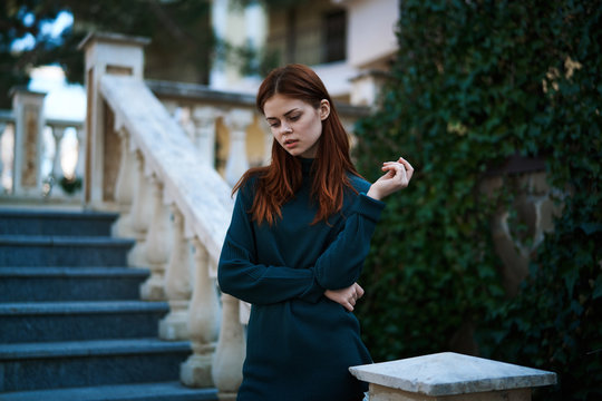 Red-haired woman standing in the street wearing a sweater, beautiful girl, architecture