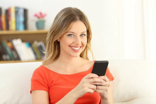 Girl looking at camera holding a smart phone at home