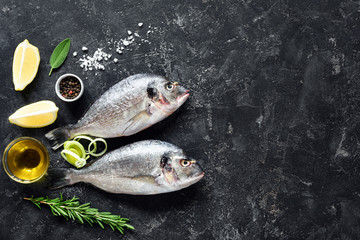 Fresh fish Sea Bream, Herbs, Spices, Olive oil and Cooking ingredients on Stone Slate Background. Top view. Fish ready for cooking. Copy space for your text