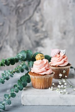 Cupcakes with coral buttercream and meringues on marble board. Wedding cupcakes. Grey concrete wall background. Vertical and copy space for text