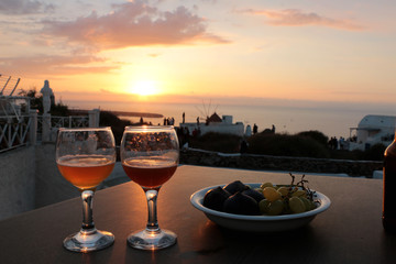 a glass of white wine and fruits on balcony with Caldera city view at sunset