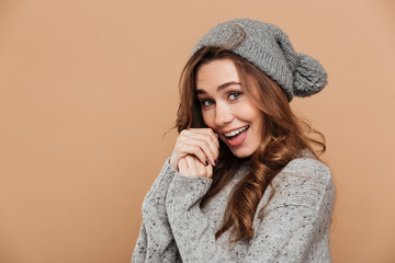 Close-up photo of cute brunette woman in gray sweater and hat warming hands and looking at camera