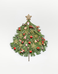 Christmas tree made with cedar branches , decorated with gold star and red festive decorations , holidays cookies and gingerbread man on white background, top view. Festive layout for greeting card