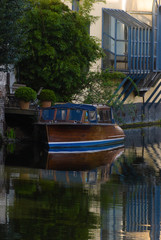 Fototapeta na wymiar Stationed wooden boat at the canal in Ghent with his reflection surrounded with green and buildings in springtime