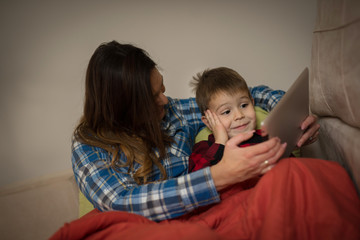 Mother and son sitting on sofa using digital tablet.