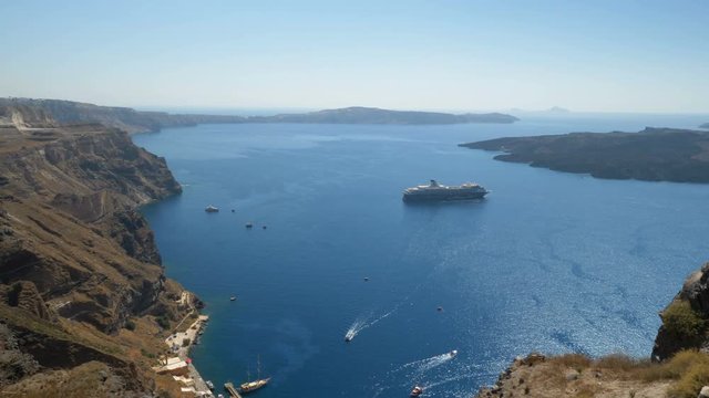 Panning shot of white buildings and cruise ships on Aegean Sea, Santorini Island, Greece. Sunny day, blue sky. Town of Fira