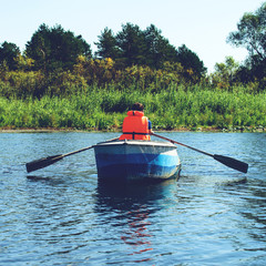 Man in life jacket rowing a boat over clear water on the river, toned image
