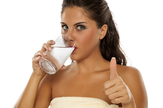 a young woman drinks cold water from the glass and showing thumbs up