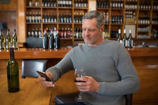 Smiling senior man using mobile phone while having red wine - Powered by Adobe