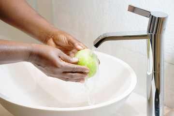  Female hands wash the apple under the tap. Woman young housewife washing fresh green apple in kitchen under water stream. Healthy eating.