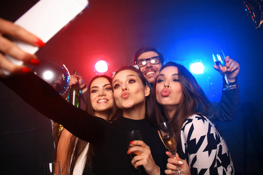 party, technology, nightlife and people concept - smiling friends with smartphone taking selfie in club.