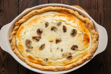 Homemade delicious quiche with mushrooms and cheese in a dish on a wooden background.
