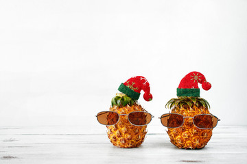 Fototapeta na wymiar Closeup of two pineapples in sunglasses and christmas hat over white background with copy space. Christmas in exotic country concept.
