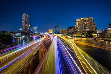 Obraz premium Light trails of boats sailing on Chao Phraya river with the skyscrapers of the financial district at night, Bangkok Thailand. Beautiful light painting.