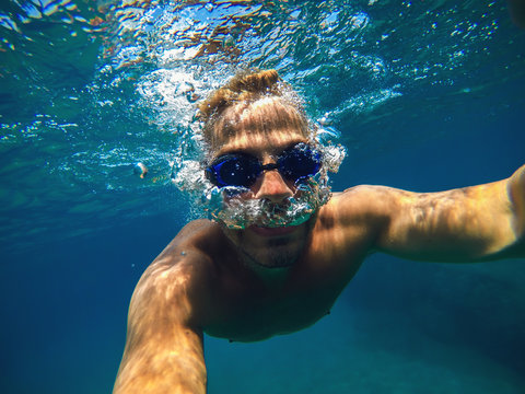 Underwater view of a young diver man swimming in the turquoise sea for summer vacation while taking a selfie.