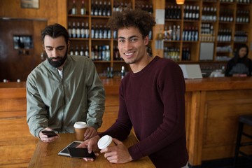 Two male friends using mobile phone while having coffee