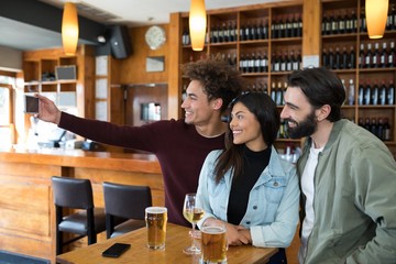 Friends taking selfie with mobile phone while having glass of