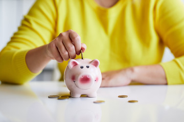 Close up of female hand putting coin into piggy bank