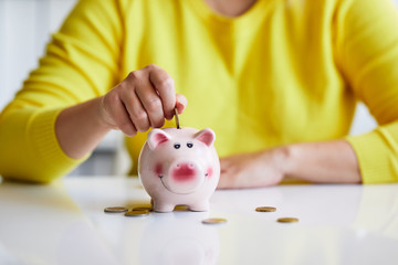 Obraz na płótnie Canvas Close up of female hand putting coin into piggy bank