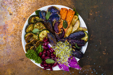 Baked and raw vegetables with herbs served on white plate.

