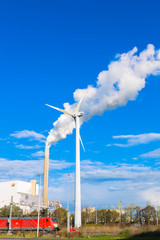  A wind turbine and a factory pipe with smoke.