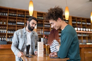 Two male friends looking at wooden blocks while having beer