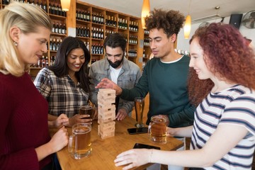 Friends playing with wooden blocks while having glass of beer