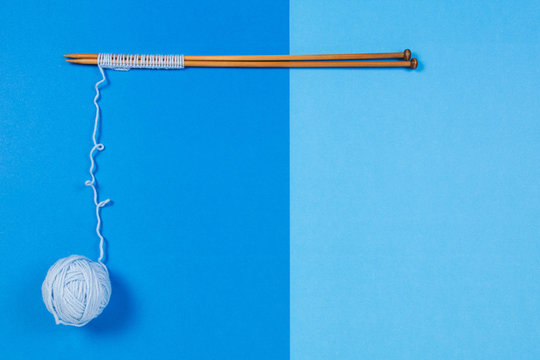 Wooden knitting needles and small yarn ball on blue background.