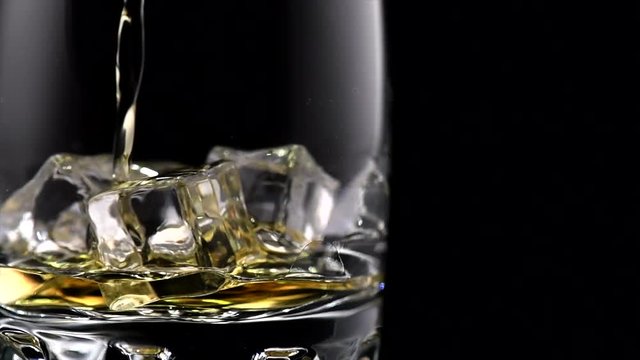 Whisky on the rocks. Whiskey pouring in a glass with ice isolated on black background. 4K UHD video 3840x2160