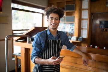 Smiling waiter using mobile phone at counter