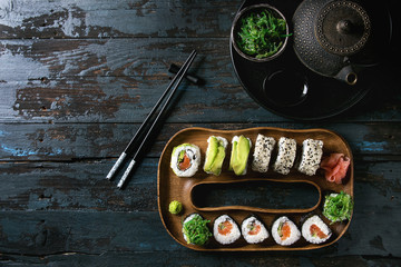 Homemade sushi rolls set with salmon, sesame seeds and avocado serving in wood plate with pink...